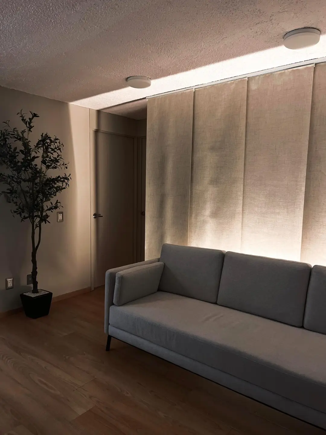 Sala con sillón gris y panel de lino iluminado con luz cálida
